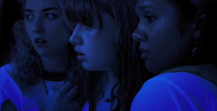 Image: A nighttime image of three women in profile looking off into the distance with concerned looks on their faces.