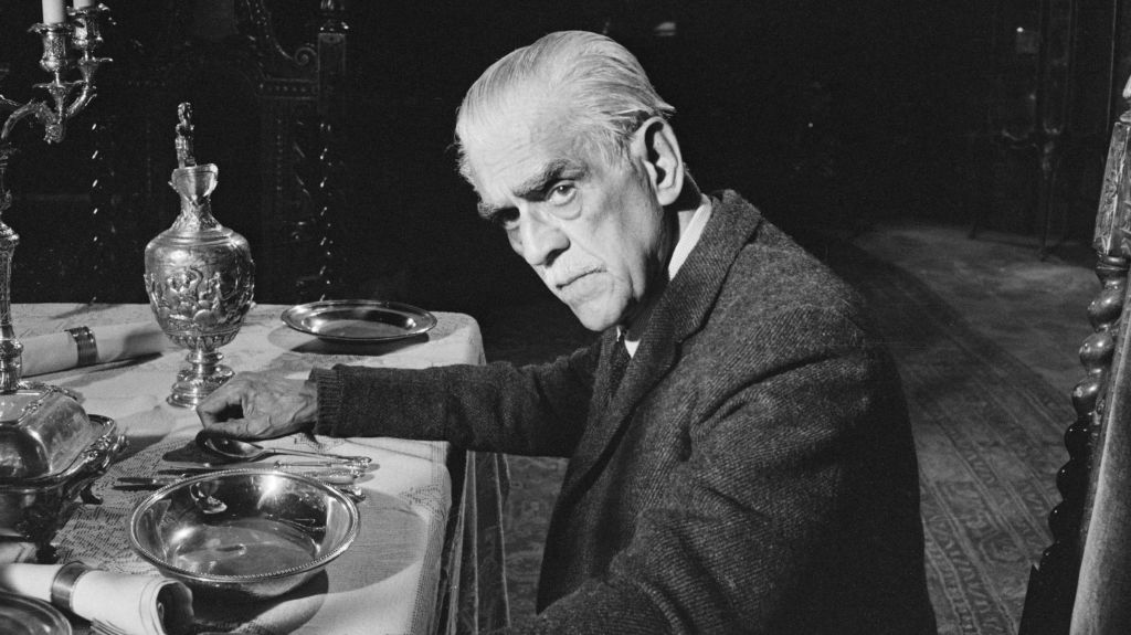 A photo of an older Boris Karloff seated at an elaborate dining table.