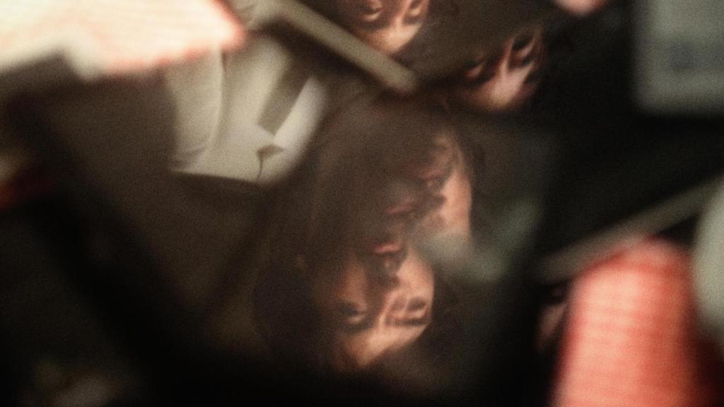 A still from Horse Brothers. A pile of broken phones and tablets lie on a table. A brother's face is reflected in the electronics. 