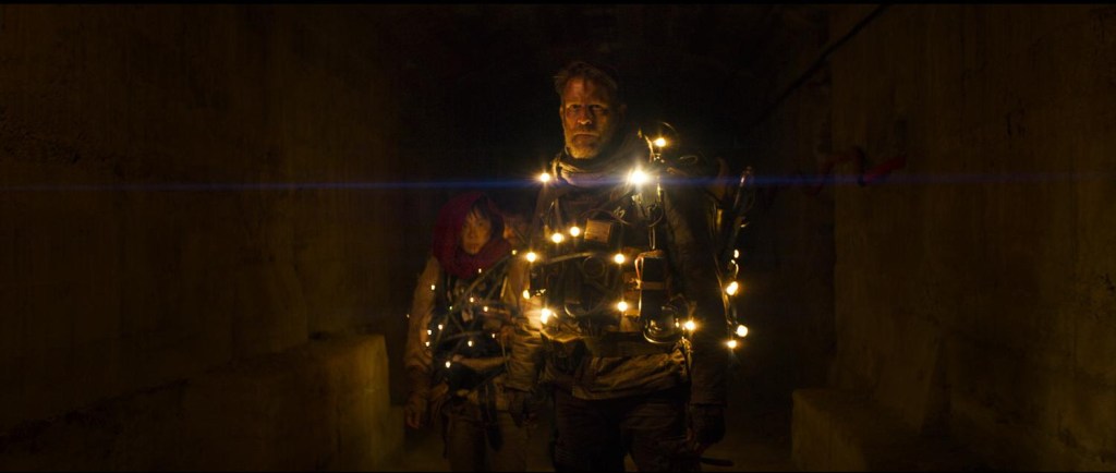 A still from Night Breakers. People wearing suits made of stringed lights stand in a dark tunnel. They look forward warily. 