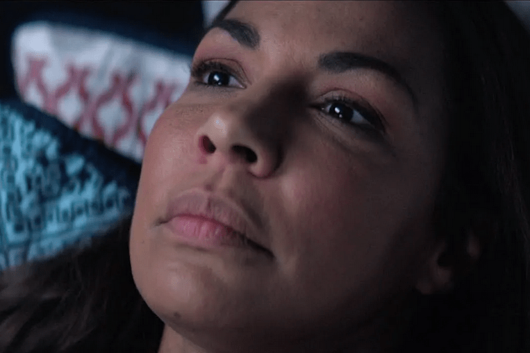 A still from Ashgrove. A close-up shows Jennifer lying on a bed deep in thought. 