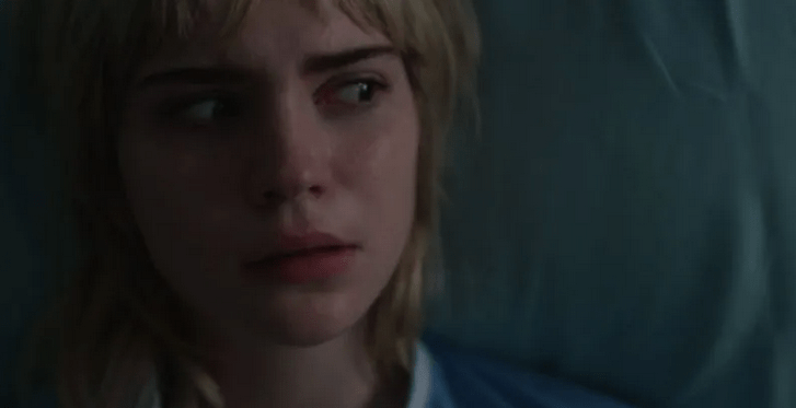 A still from Blink. Mary lies in a hospital bed looking off to the side in terror. 