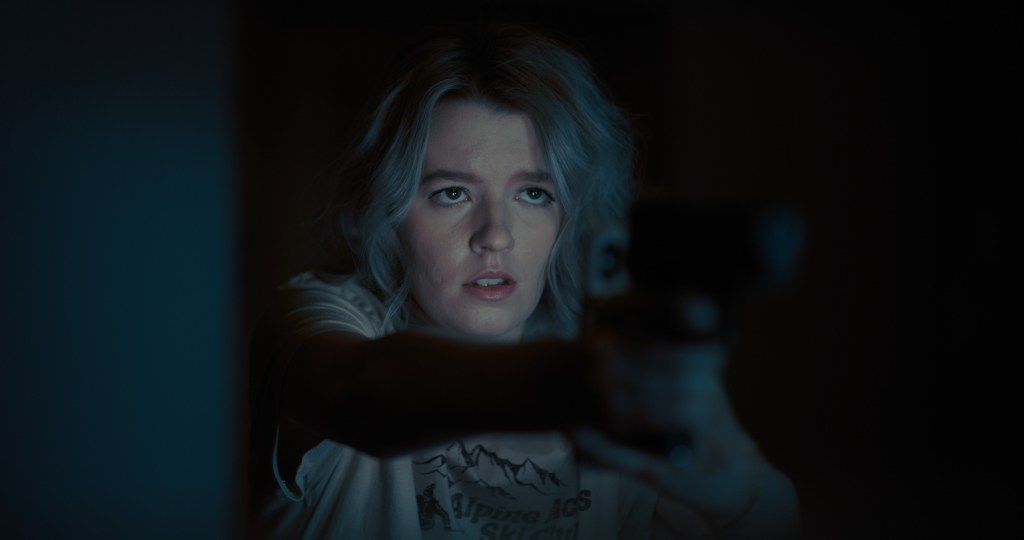 A still from See for Me. Sophie holds a gun out in front of her with the light from a cell phone illuminating her tense face.