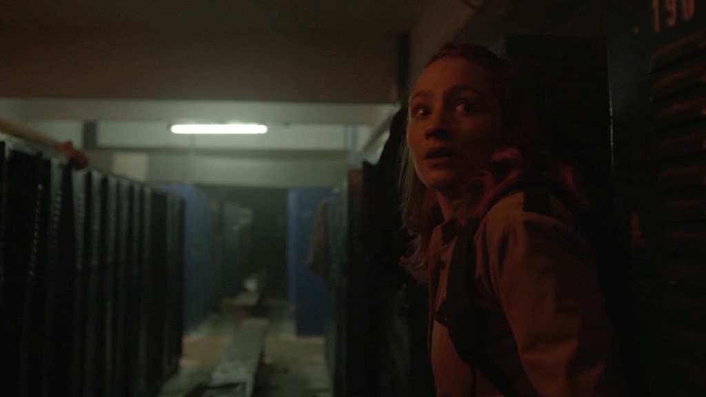 A still from Virus :32. Iris stands in a locker room, looking behind her in fear. 