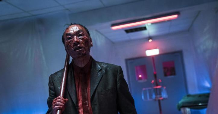 A still from The Sadness. The Businessman, covered in blood, carries an axe through an empty hospital hallway. 