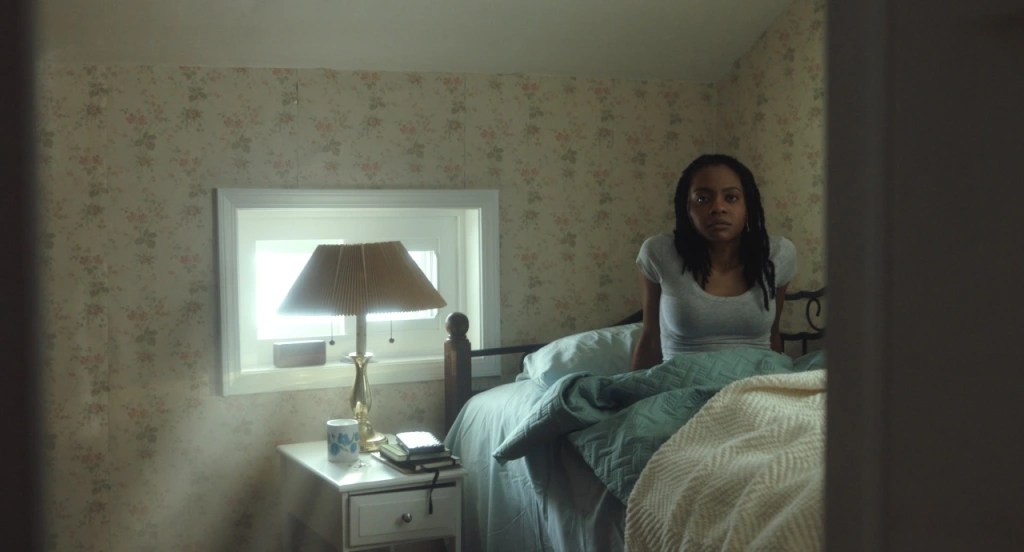 A still from The Harbinger. Monique sits up in bed as sunlight comes in through a window.