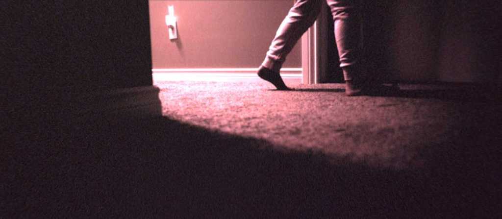 A still from Skinamarink. A child's legs walk down a hallway lit by a nightlight.